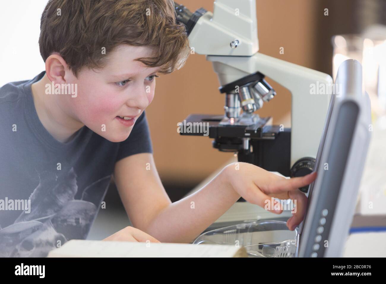 Studente ragazzo che conduce esperimenti scientifici al microscopio e al computer in classe di laboratorio Foto Stock