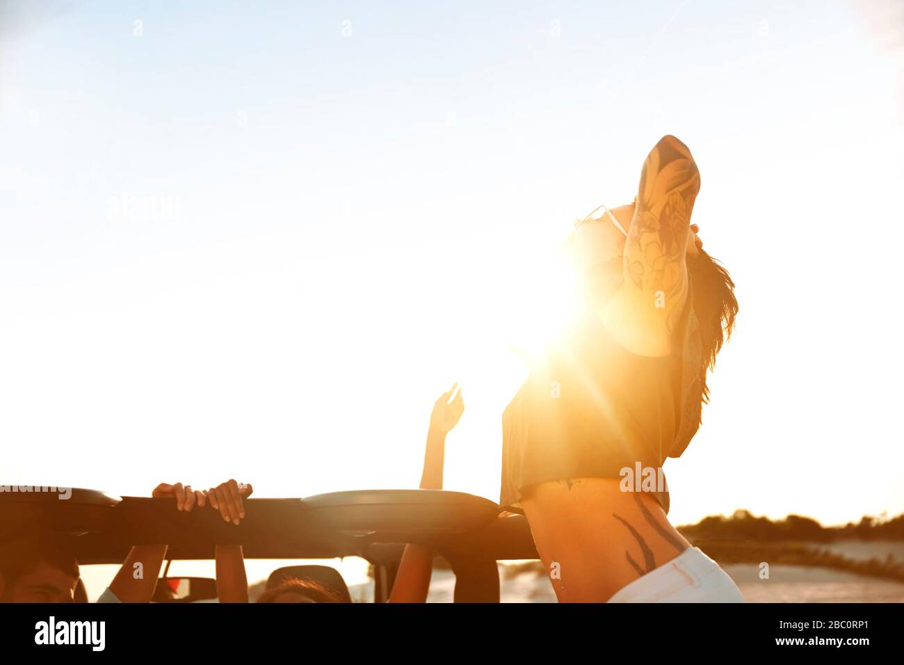 Giovane donna esuberante con tatuaggi sulla spiaggia soleggiata Foto Stock