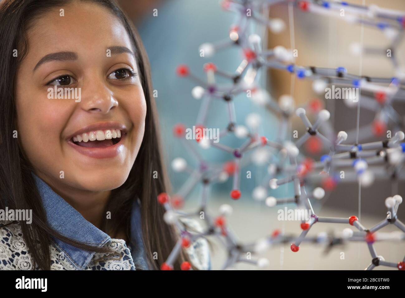 Curioso, sorridente studentessa studentessa che esamina la struttura molecolare Foto Stock