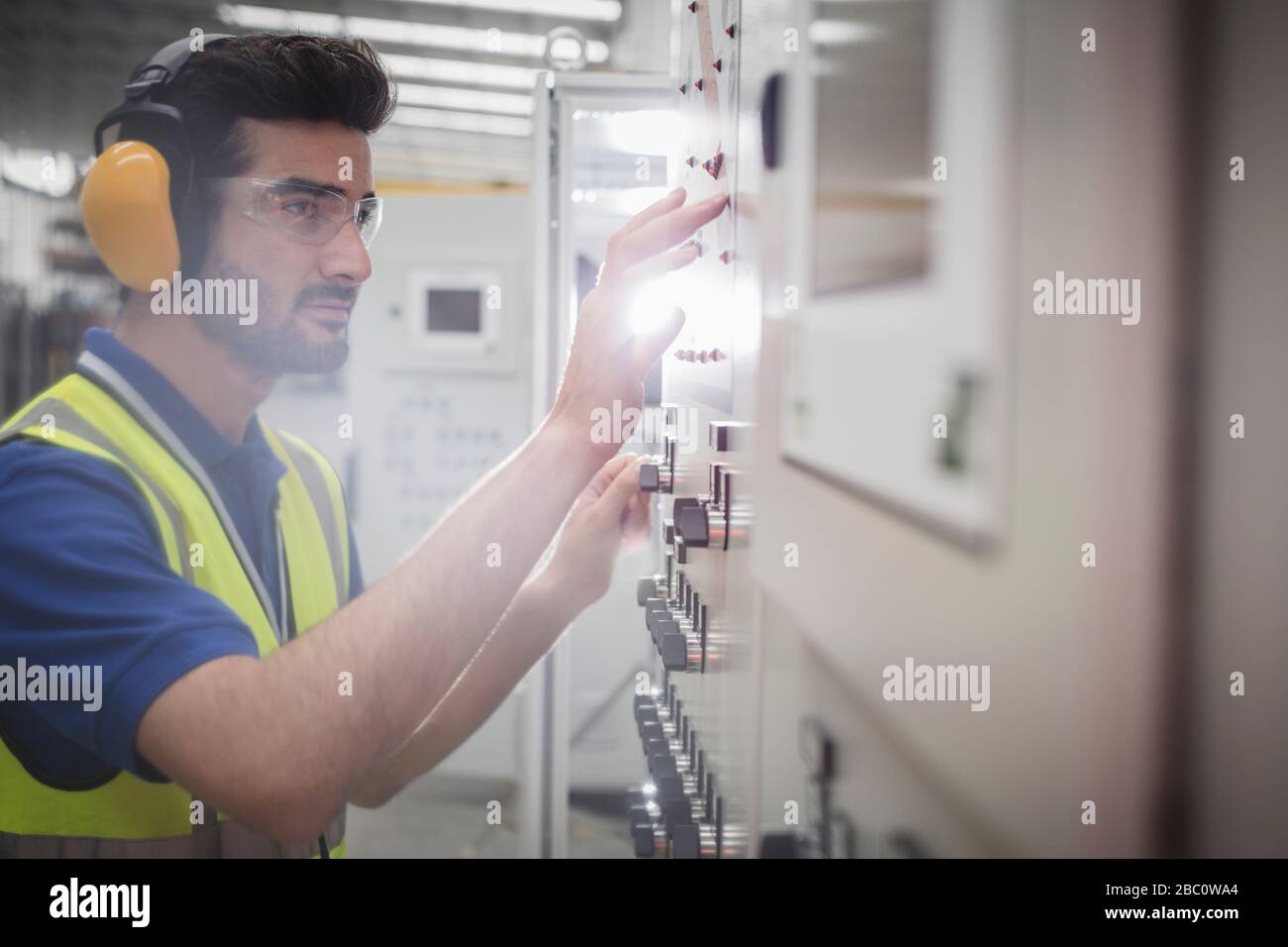 Lavoratore maschio che indossa protezioni per le orecchie, che utilizza macchinari presso il pannello di controllo in fabbrica Foto Stock