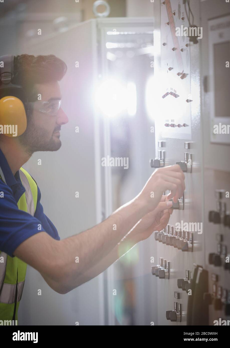 Lavoratore maschio che indossa protezioni per le orecchie, che utilizza macchinari presso il pannello di controllo in fabbrica Foto Stock