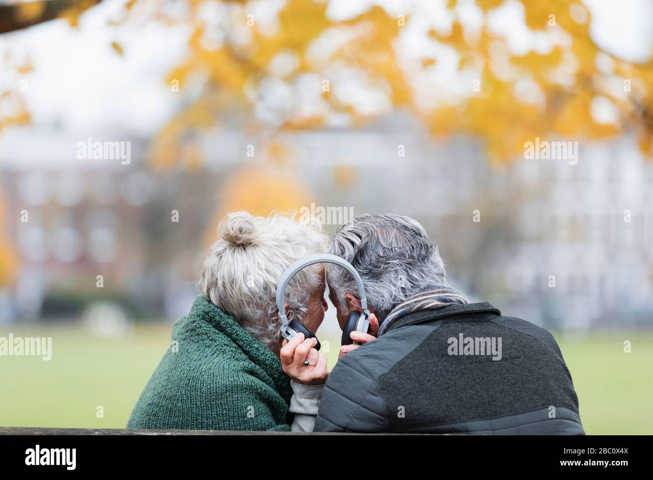 Coppia senior che condivide le cuffie, ascoltando musica nel parco autunnale Foto Stock