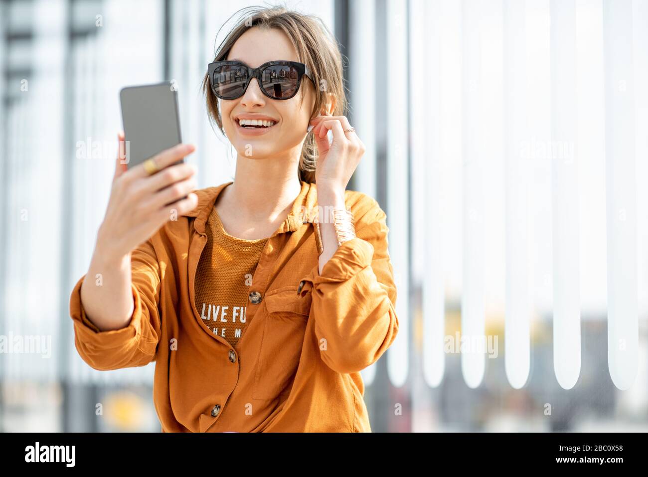 Giovane donna che ha una videochiamata sul telefono cellulare mentre si siede al punto di trasporto all'aperto. Comunicazione online Foto Stock