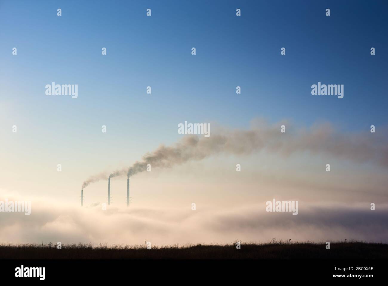 Cime di tre pile fumanti di centrale termica all'orizzonte prese dalla collina, tubi in nebbia mattutina su cielo blu, concetto di emissione pericolosa in atmosfera, ecologia, inquinamento ambientale Foto Stock