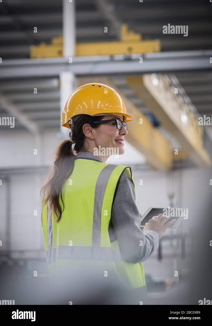 Lavoratore femminile sicuro e sorridente che utilizza un tablet digitale in fabbrica Foto Stock