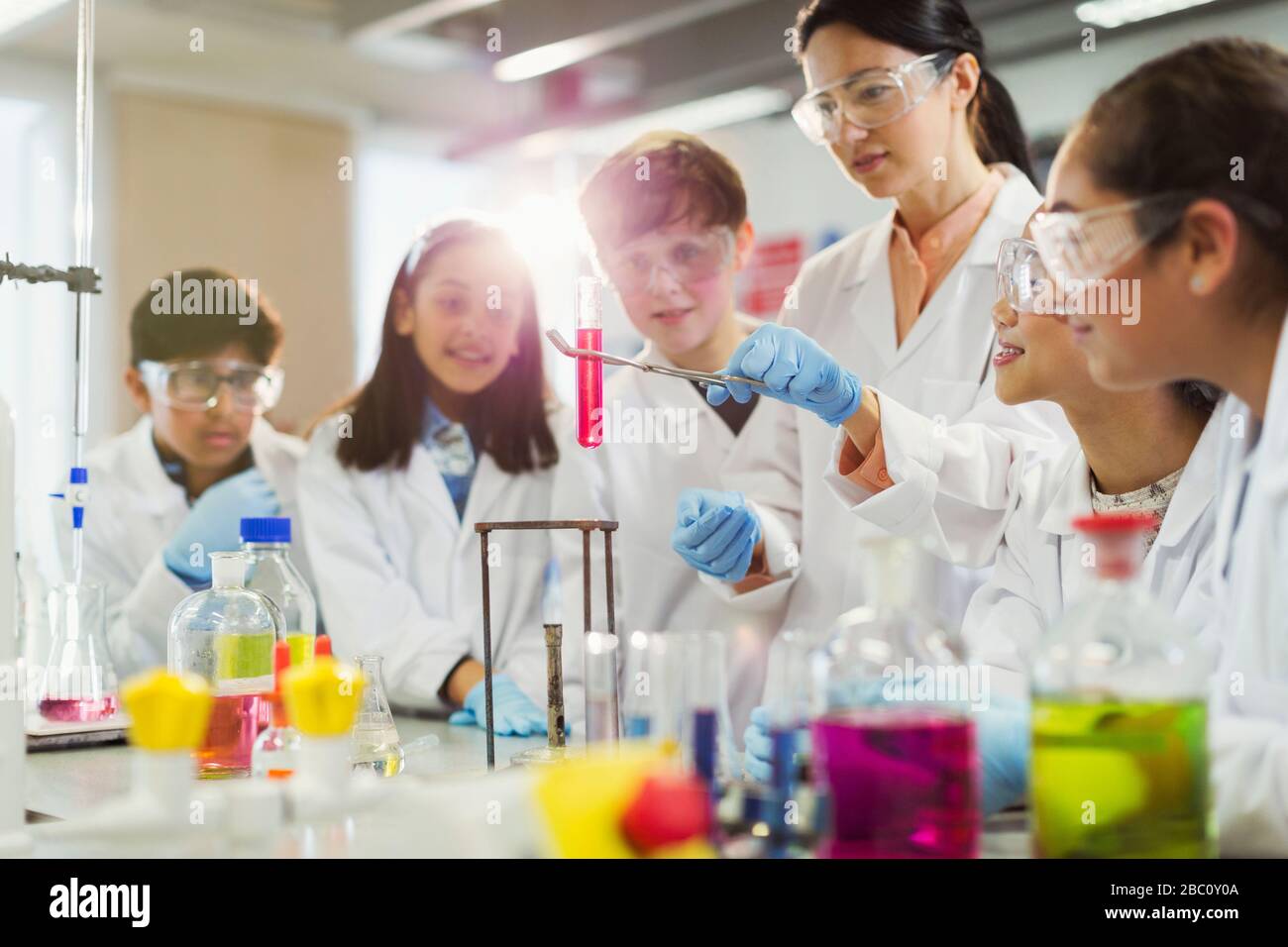 Insegnante femminile e studenti che conducono esperimenti scientifici, osservando il liquido nella provetta in classe di laboratorio Foto Stock