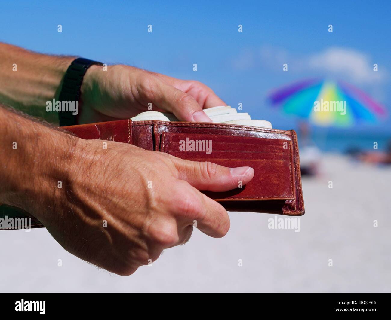 Uomo che tiene un portafoglio che mostra soldi in mano con uno sfondo spiaggia. Concetto di investimento, finanziario e di successo nel business e di spendere denaro. Foto Stock