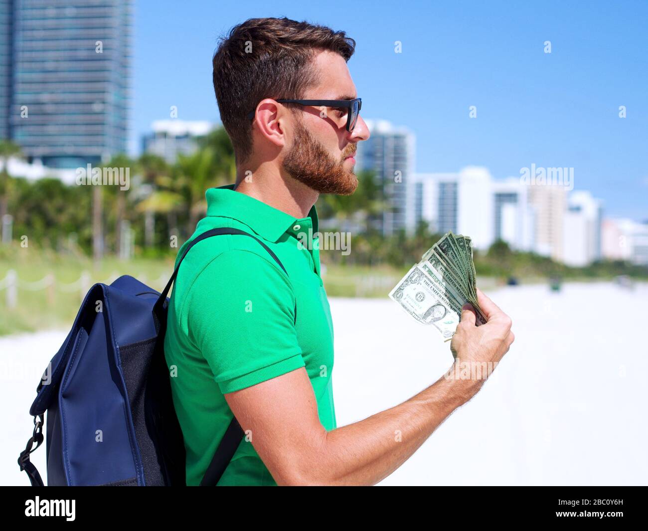 Il turista caucasico che tiene i soldi del dollaro degli Stati Uniti in mano sullo sfondo della spiaggia. Le fatture del USD nel concetto di investimento, finanziario e riuscito nel commercio un Foto Stock