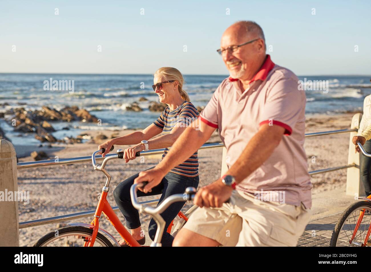 Sorridente attivo anziani turisti in bicicletta lungo l'oceano soleggiato Foto Stock
