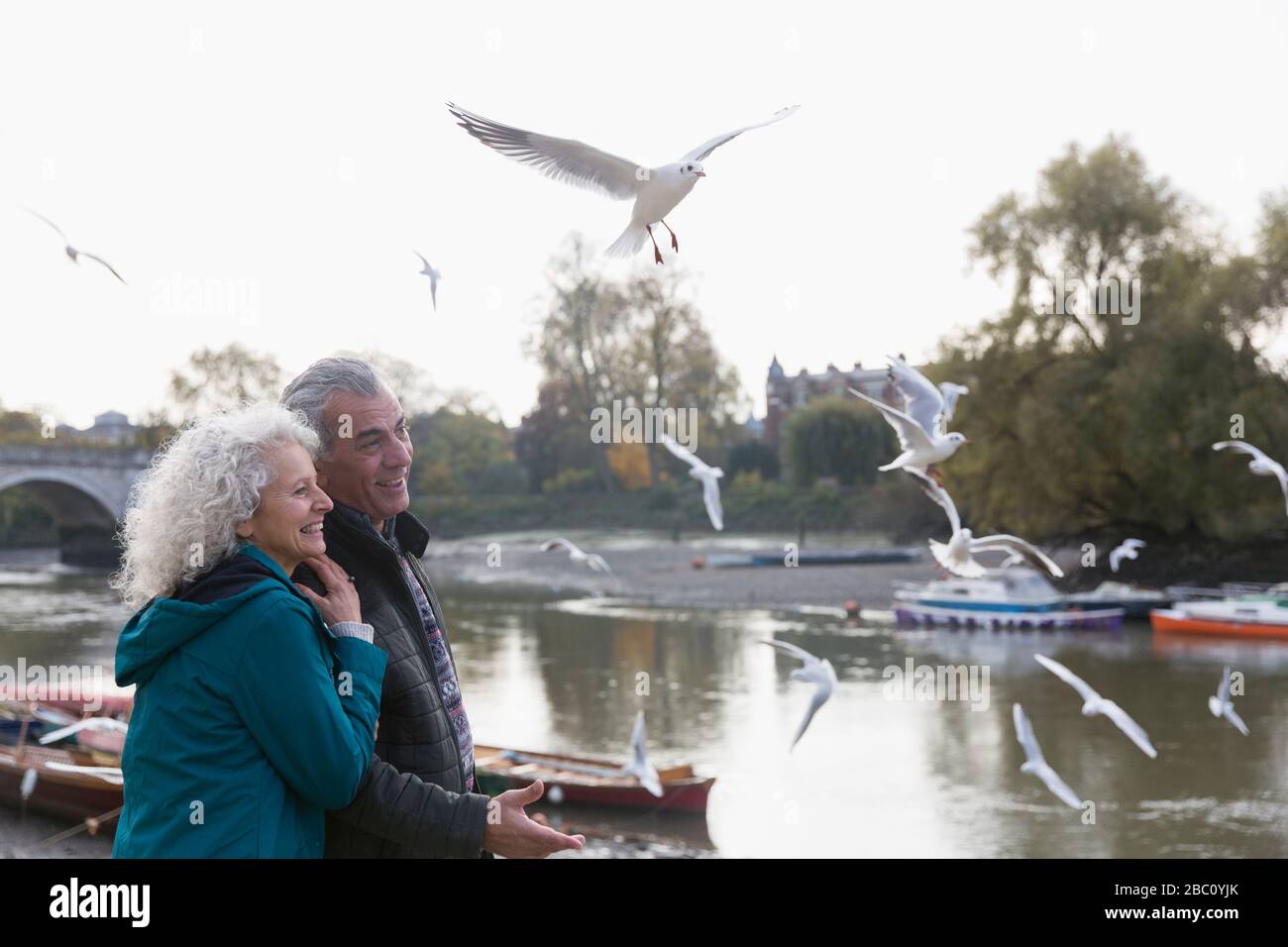 Affettuosa coppia senior guardando uccelli che volano al fiume Foto Stock