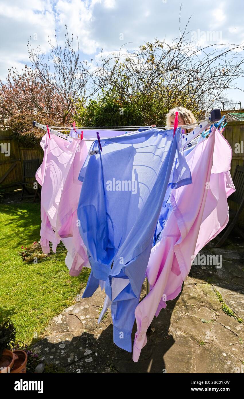 Donna che appende fuori le camicie di vari uomini colorati su una linea di lavaggio rotante durante il vento nel giardino posteriore Regno Unito Foto Stock