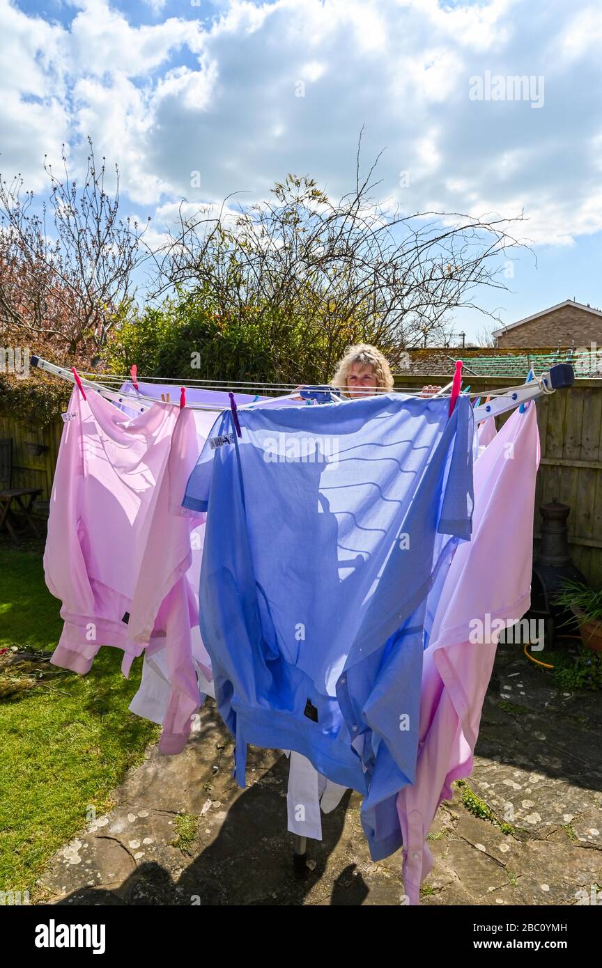 Donna che appende fuori le camicie di vari uomini colorati su una linea di lavaggio rotante durante il vento nel giardino posteriore Regno Unito Foto Stock