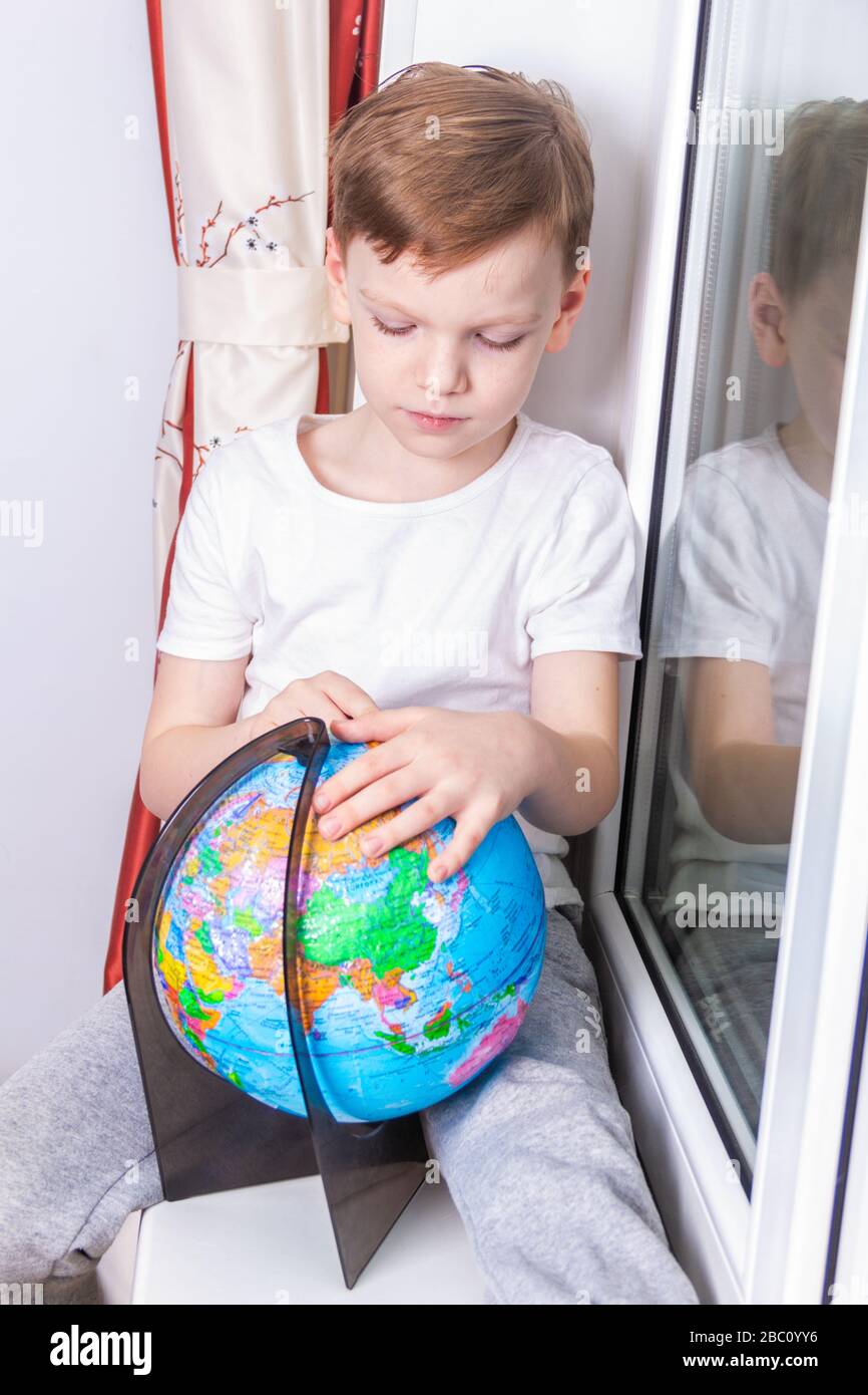 Concetto di isolamento e quarantena. Un ragazzo di sette anni in quarantena studia il globo e sogna di viaggiare Foto Stock
