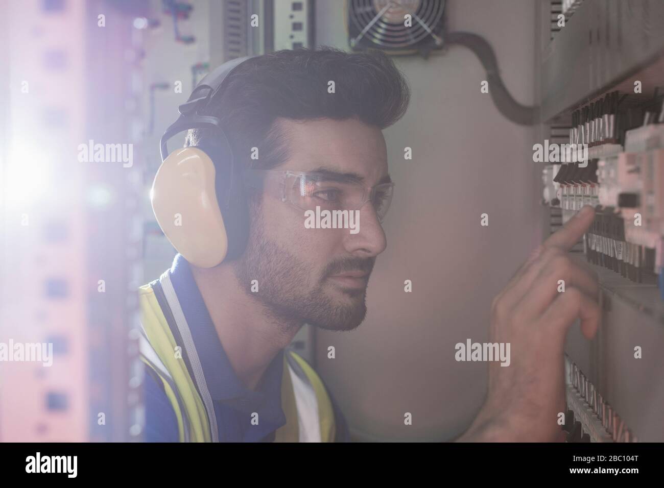 Lavoratori seri che indossano protezioni per le orecchie che utilizzano macchinari sul pannello di controllo in fabbrica Foto Stock