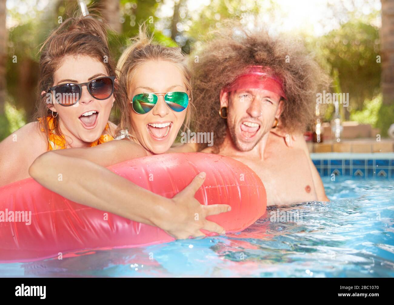 Ritratto esuberante, giocoso giovani amici con gommone nella piscina estiva Foto Stock