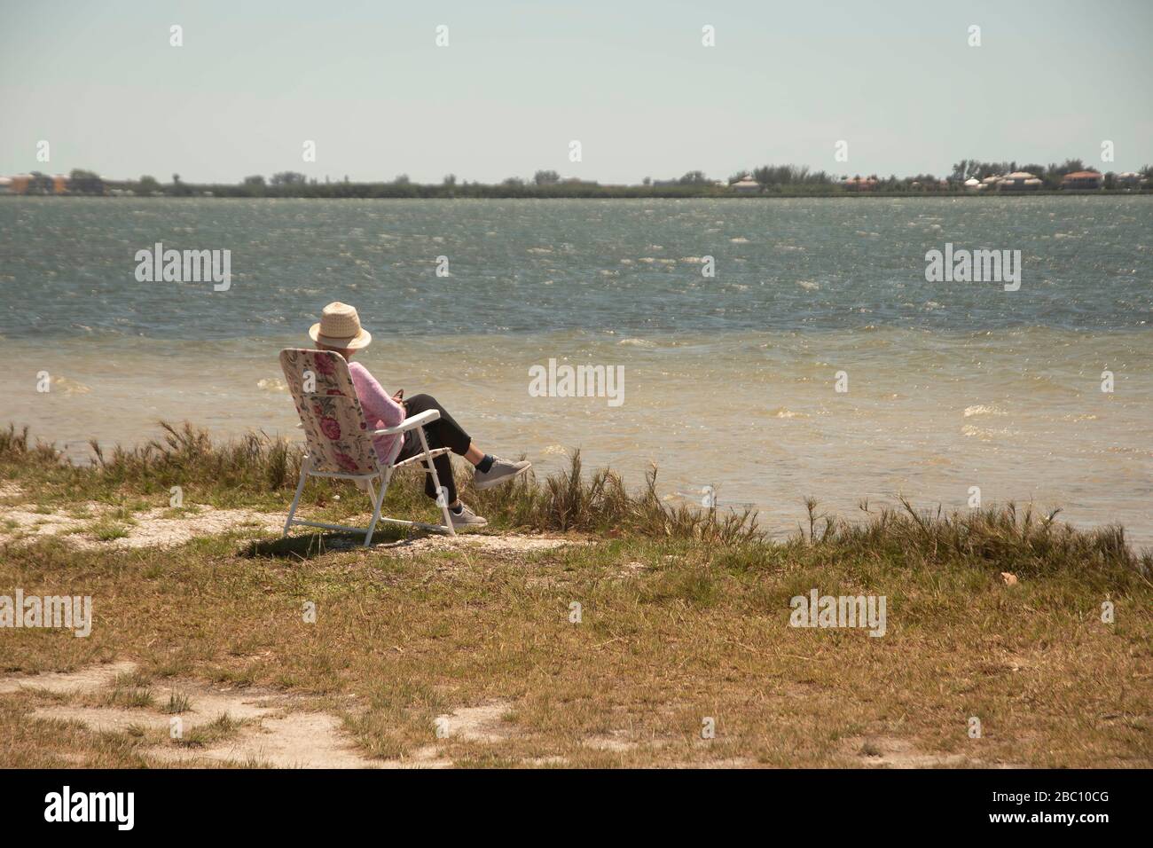 Una donna solista pratica la distanza sociale mentre siede nella sua sedia all'Indian Mound Park in Englewood, Florida, USA mentre si affaccia Lemon Bay. Florida' Foto Stock