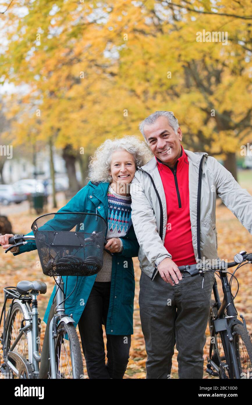 Ritratto sorridente, spensierato coppia senior con biciclette in parco autunnale Foto Stock