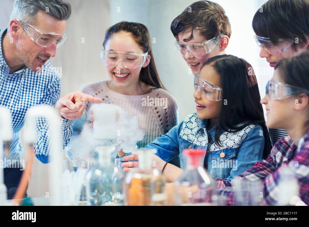 Insegnante di sesso maschile e studenti che osservano la reazione chimica, conducendo esperimenti scientifici in classe di laboratorio Foto Stock