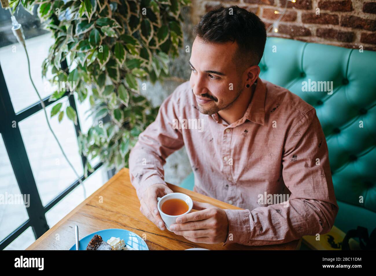 Uomo in un caffè con una tazza di tè che guarda fuori dalla finestra Foto Stock