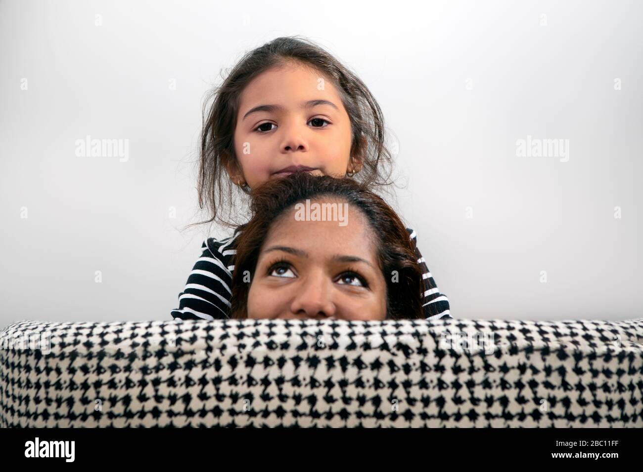 Ritratto di bambina e di sua madre che si nasconde dietro il sostegno posteriore della sedia del salotto Foto Stock