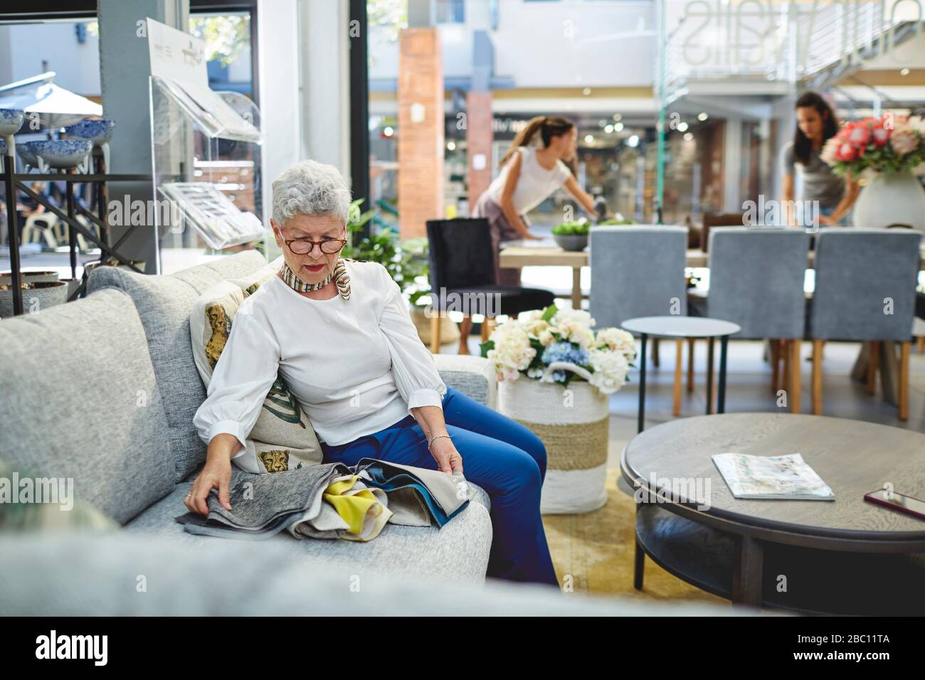 Donna anziana che guarda i campioni di tessuto sul divano nel negozio di arredamento Foto Stock