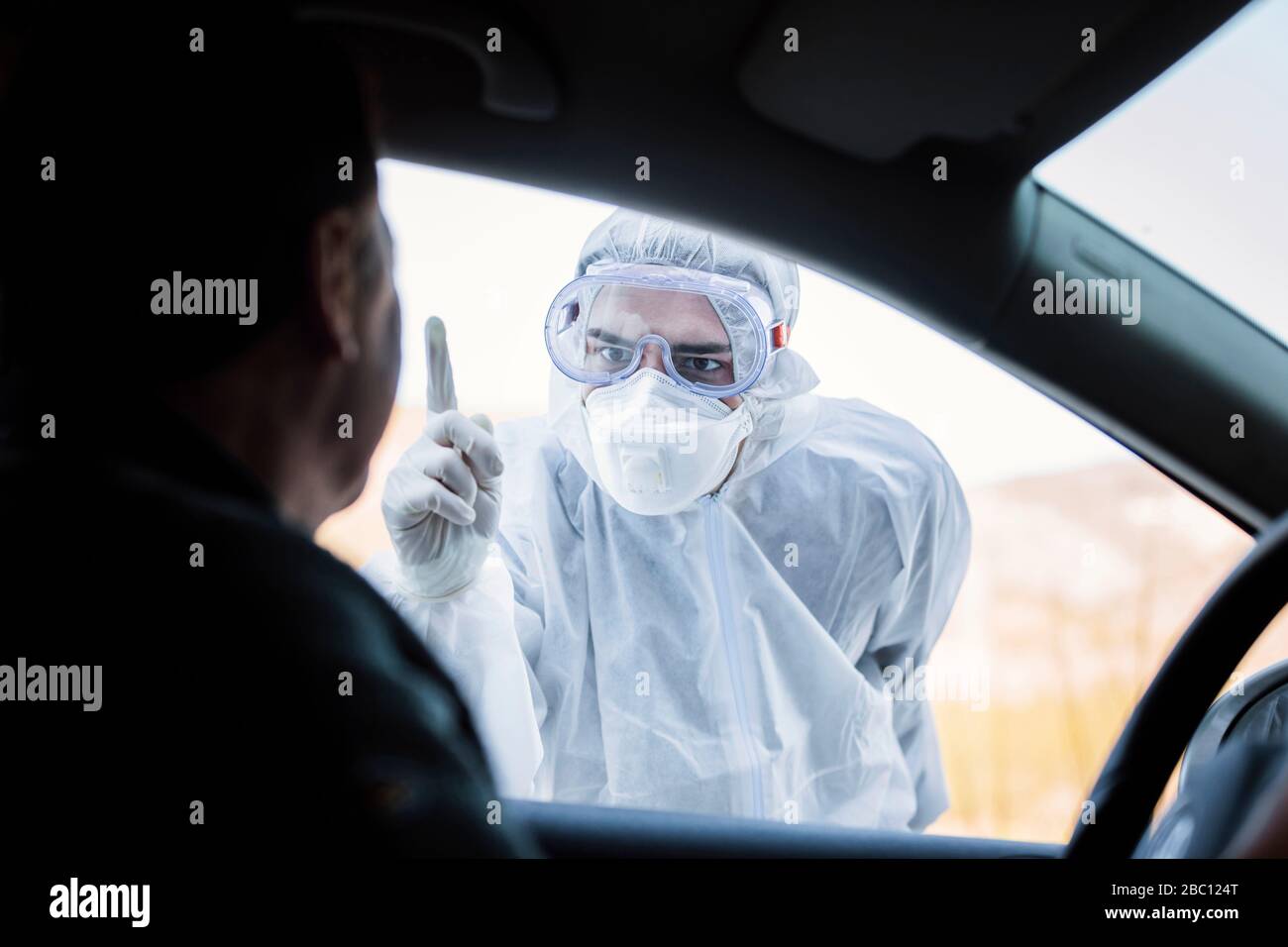 Uomo che indossa indumenti protettivi che rimprovero l'uomo anziano in auto Foto Stock