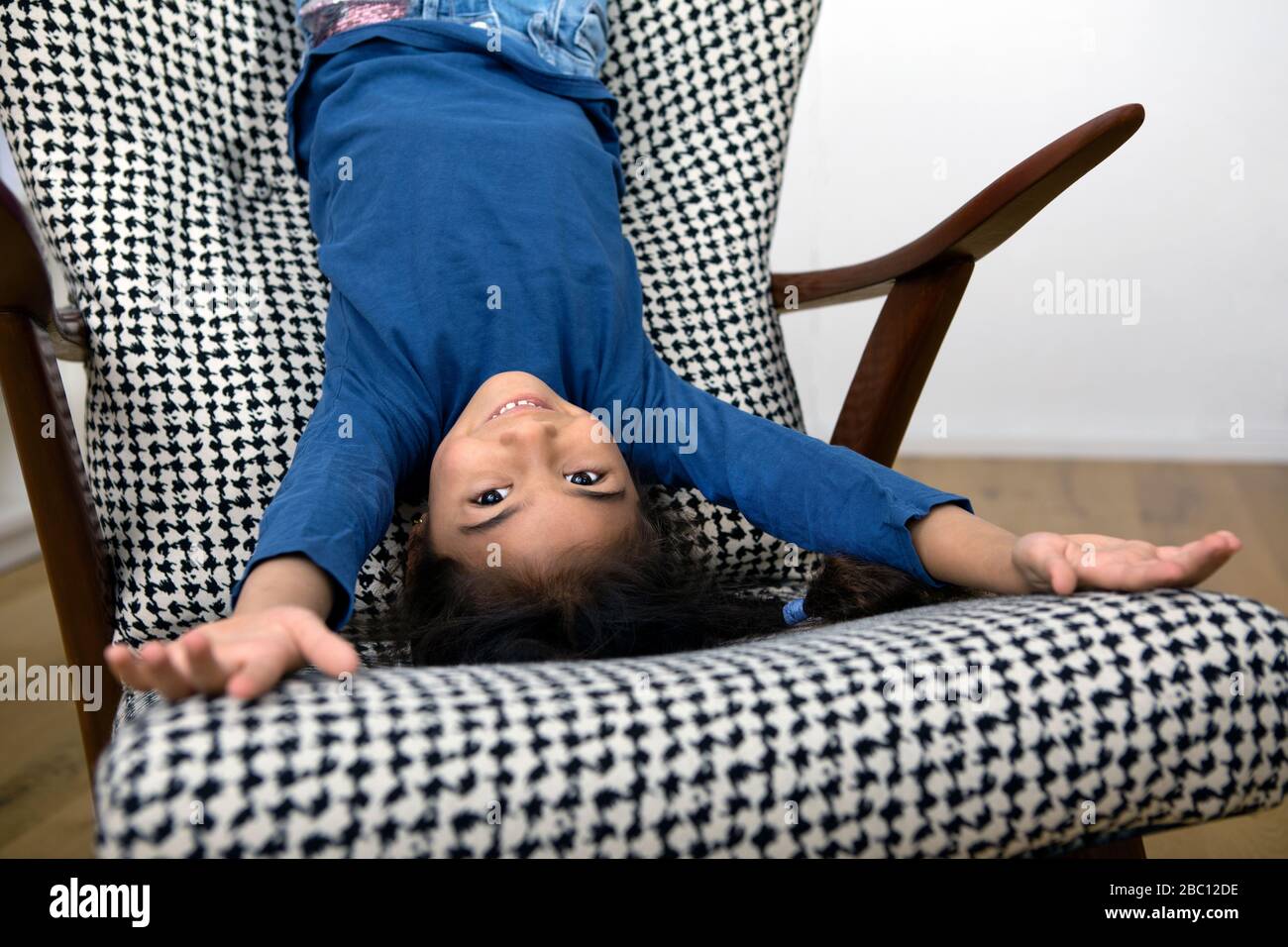 Ritratto di bambina appesa capovolta dallo schienale di una poltrona Foto Stock
