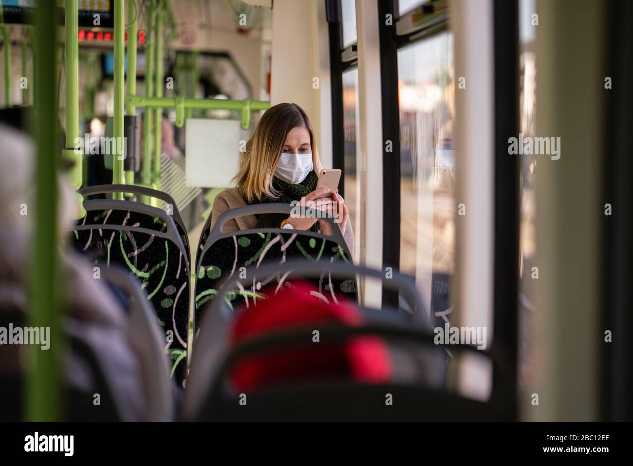 Donna con maschera facciale seduta in tram, utilizzando lo smartphone Foto Stock