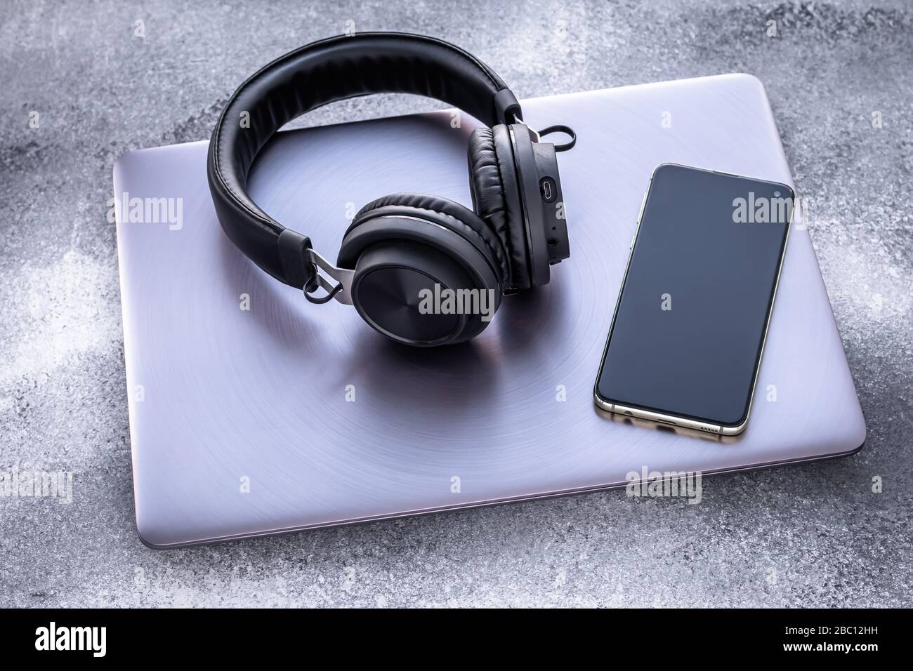 Notebook in metallo viola, cuffie portatili nere e telefono cellulare su sfondo grigio grunge. Isolamento sociale, stile di vita Foto Stock