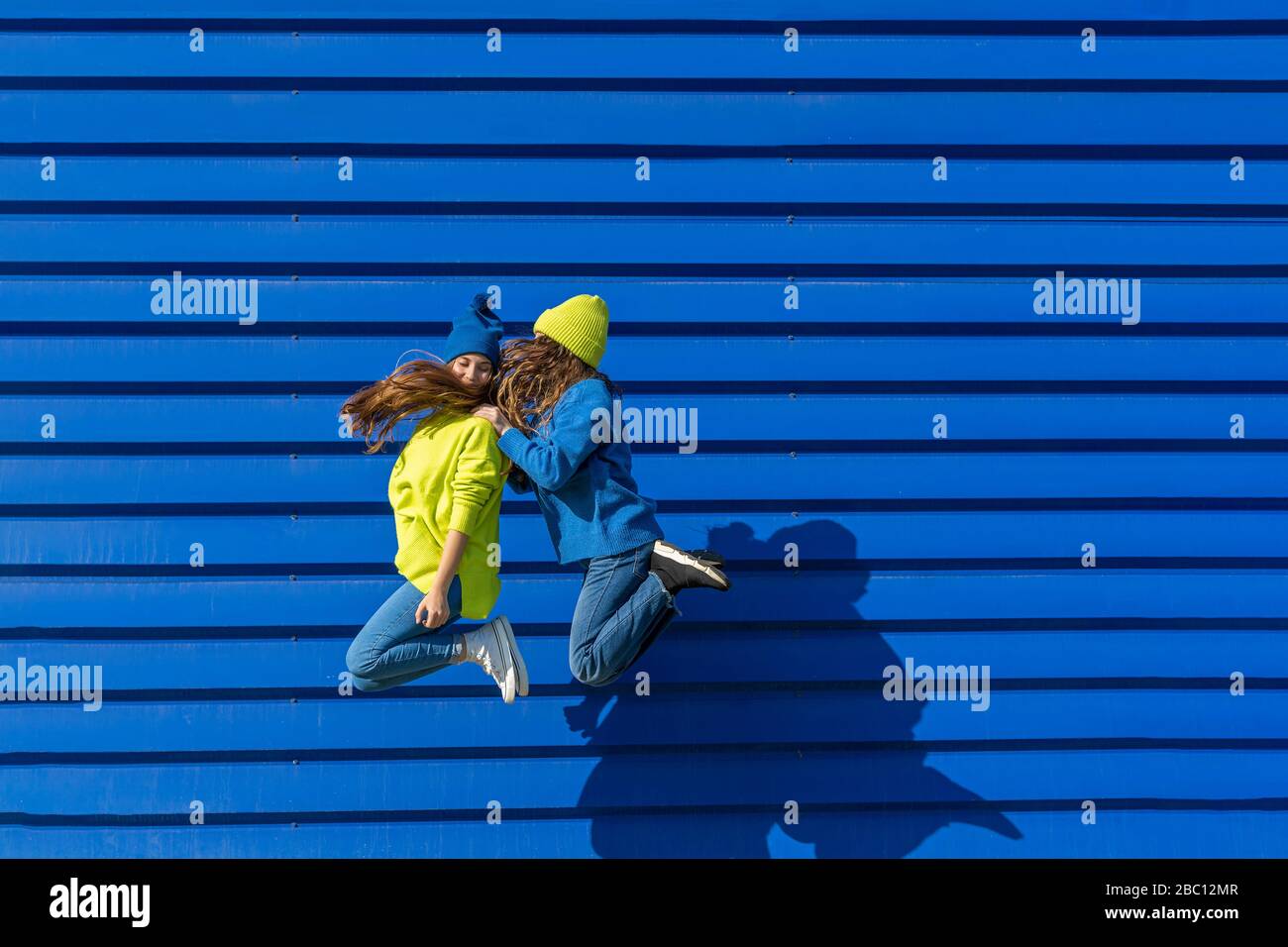 Due adolescenti che indossano abiti abbinati che saltano in aria di fronte a sfondo blu Foto Stock