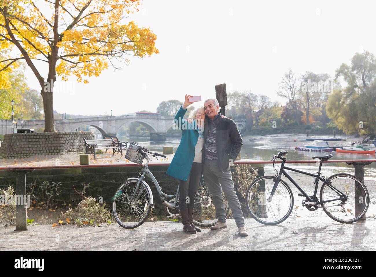 Coppia senior con biciclette che prendono selfie in autunno fiume Foto Stock