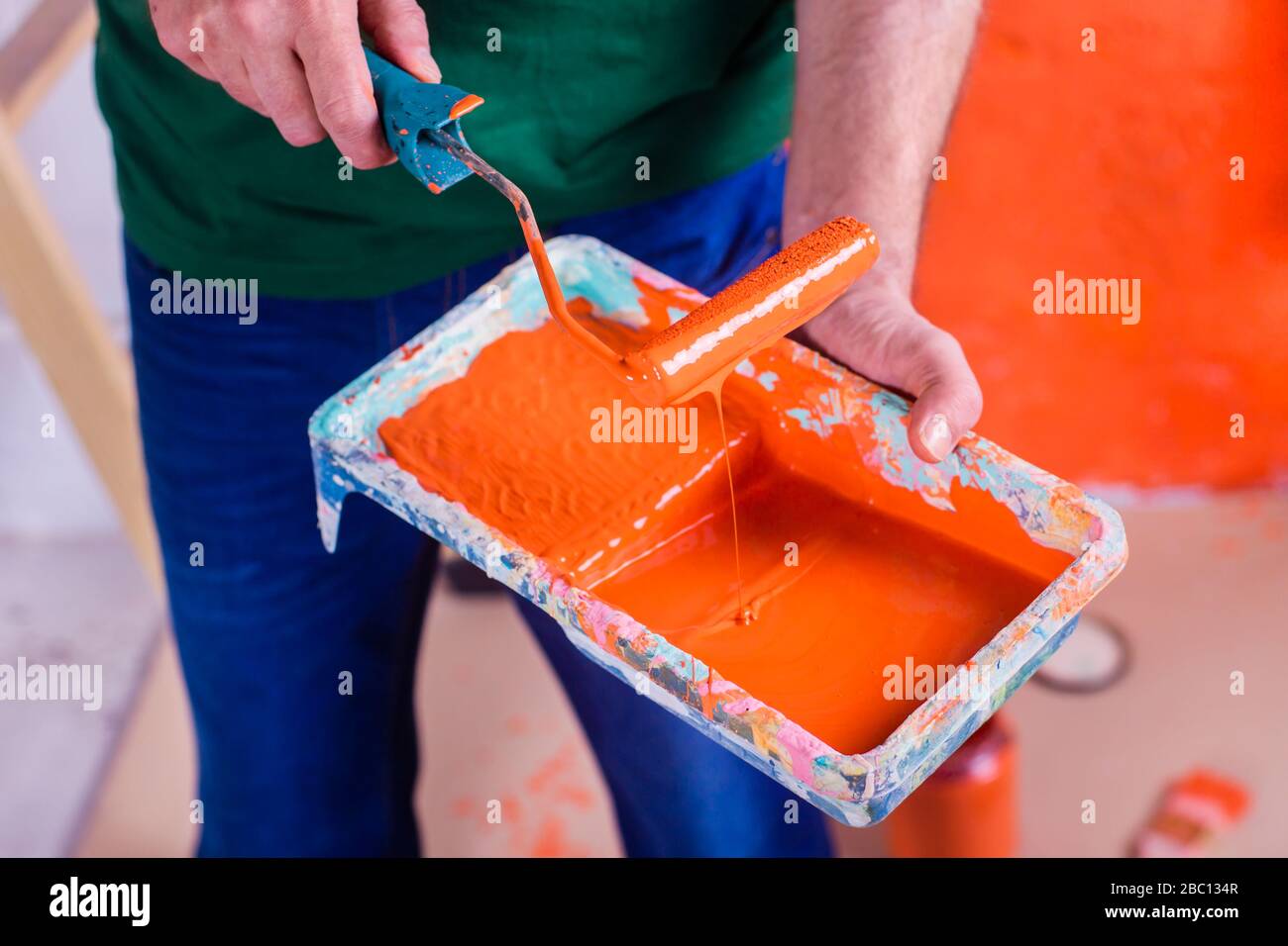 Primo piano di uomo che tiene vassoio vernice con vernice arancione Foto Stock