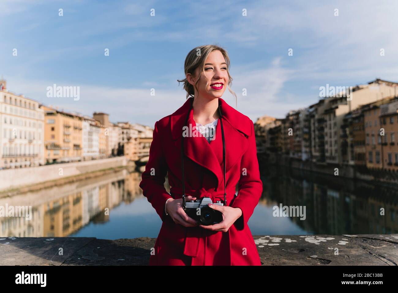Giovane donna con una telecamera in piedi su un ponte sopra il fiume Arno, Firenze, Italia Foto Stock