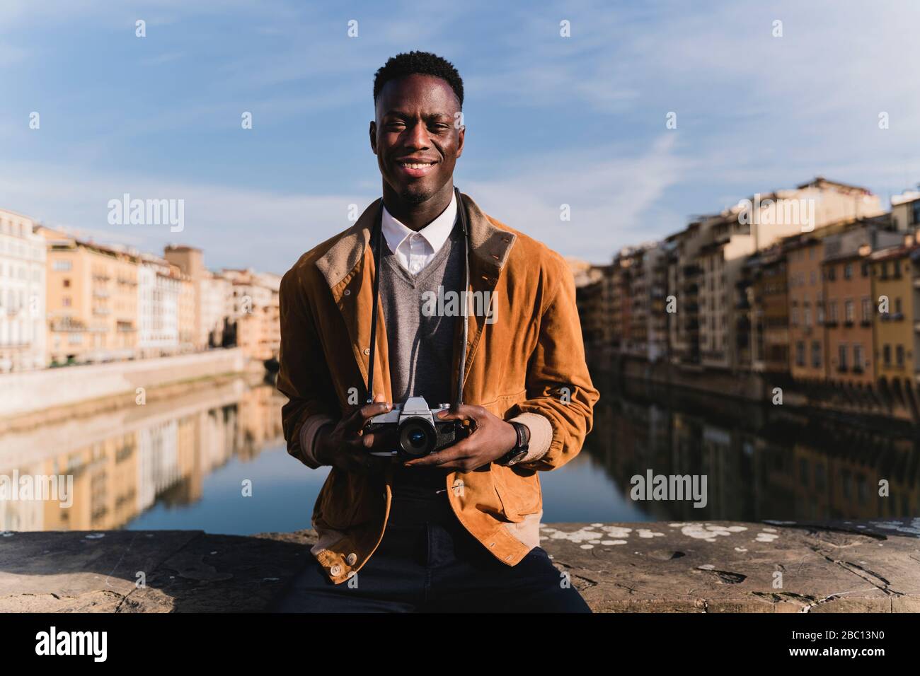 Ritratto di giovane sorridente con una macchina fotografica su un ponte sopra il fiume Arno, Firenze, Italia Foto Stock