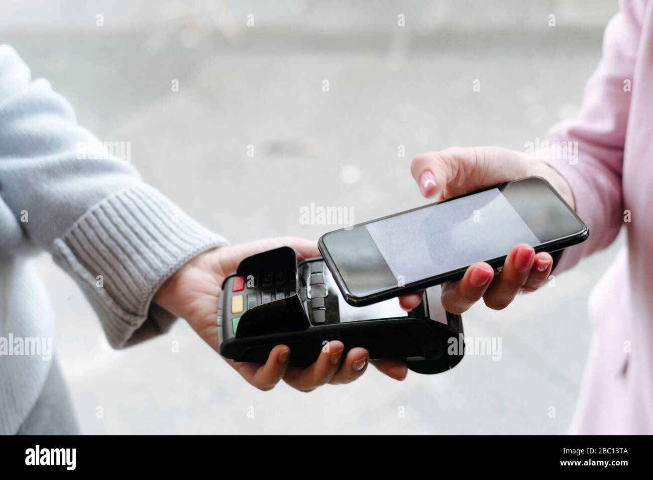 Mano di donna, pagando senza contanti al terminale POS con il suo smartphone Foto Stock