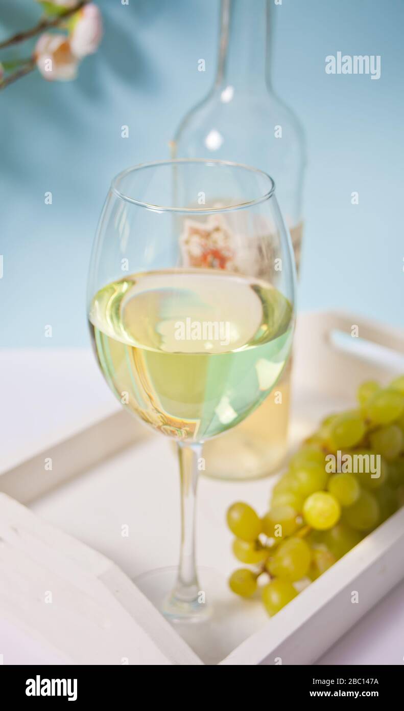 Bicchiere e bottiglia con vino bianco con uve sotto un ramo in fiore. Romantico concetto di cena primaverile Foto Stock