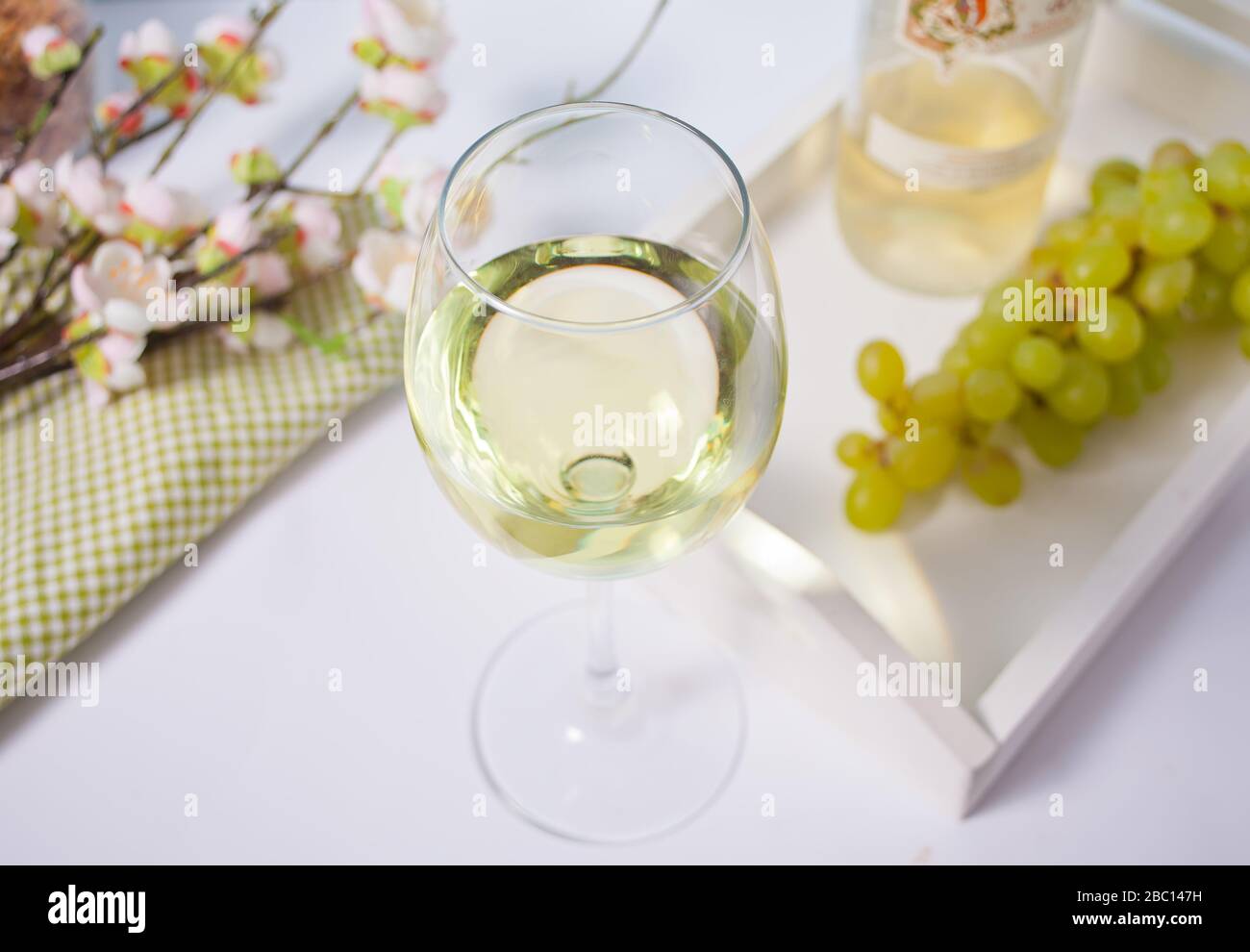 Bicchiere e bottiglia con vino bianco con uve sotto un ramo in fiore. Romantico concetto di cena primaverile Foto Stock