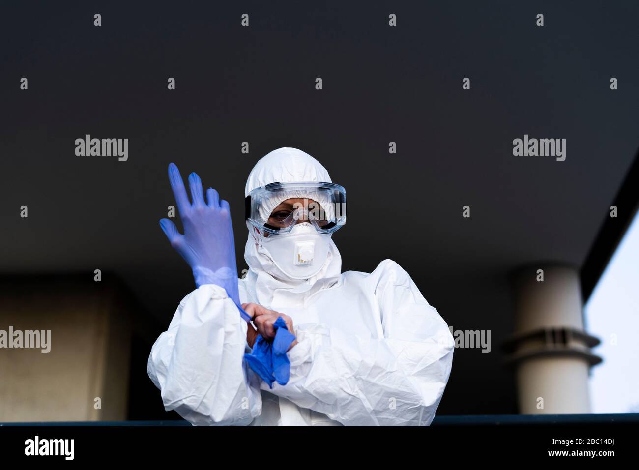 Scienziato femminile che indossa tuta e maschera di protezione e indossa guanti di protezione Foto Stock