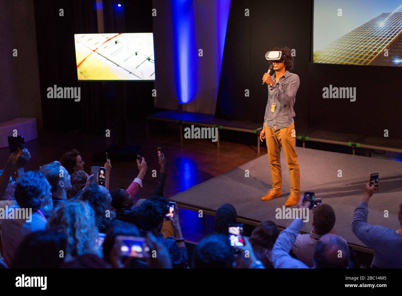 Il pubblico guarda il diffusore maschio con occhiali simulatori di realtà virtuale sul palco Foto Stock