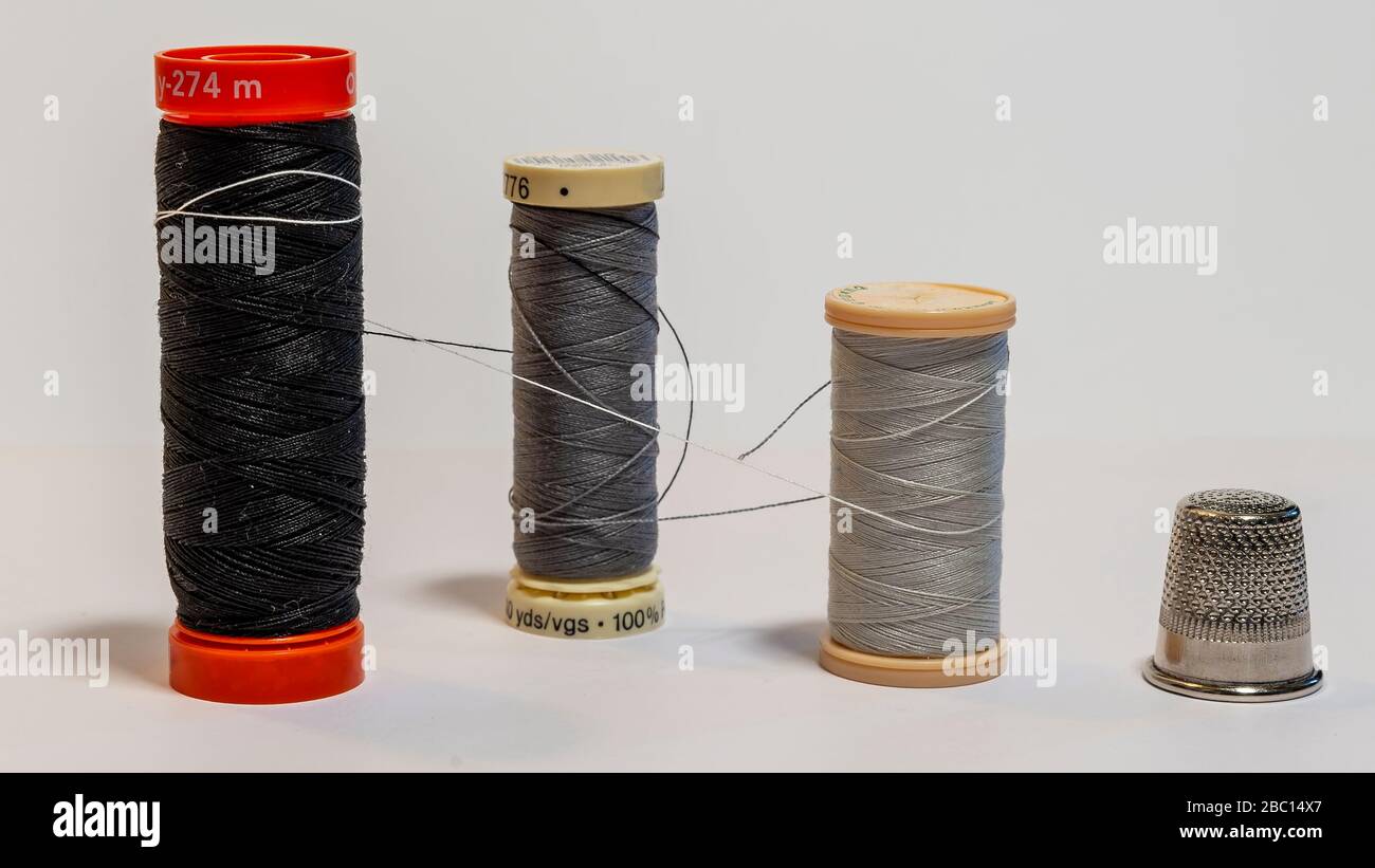 Composizione di tre rocchetti di filo per cucire legati insieme come un abbraccio e un ditale da dressaker Foto Stock