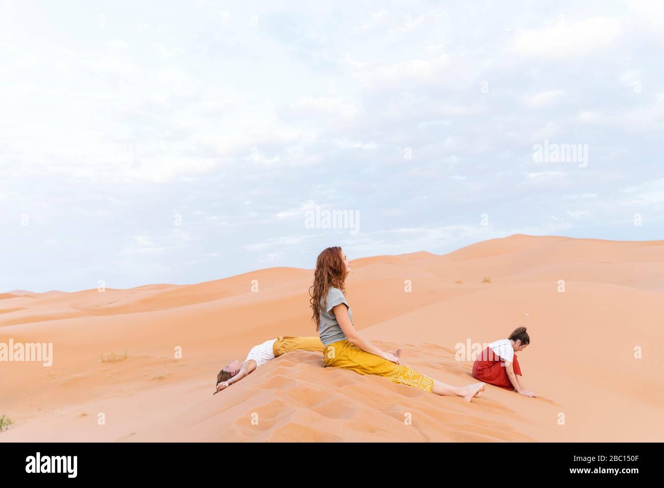 Tre giovani donne che riposano in dune di sabbia nel deserto del Sahara, Merzouga, Marocco Foto Stock