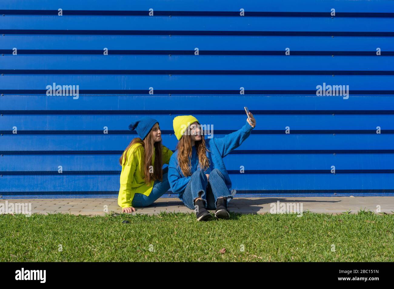 Due ragazze adolescenti che indossano abiti abbinati che portano selfie con smartphone davanti a sfondo blu Foto Stock