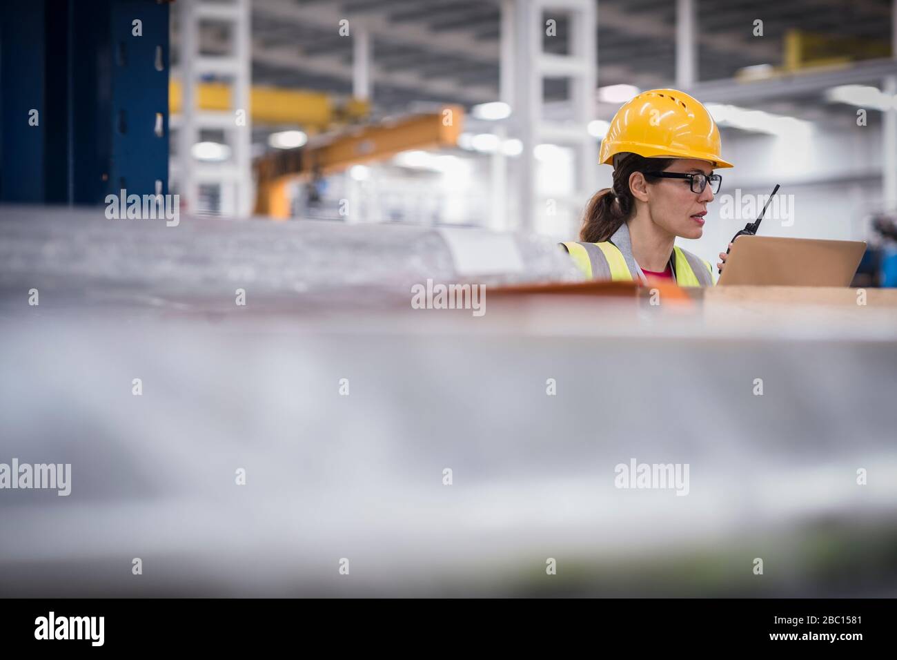 Lavoratore femminile che utilizza notebook e walkie-talkie in fabbrica Foto Stock