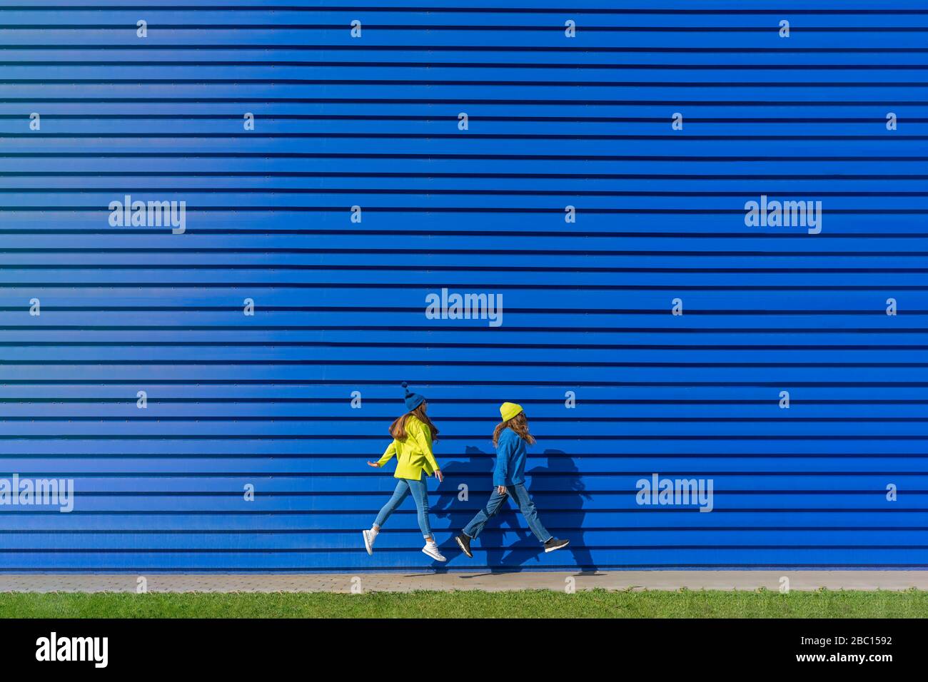 Due ragazze adolescenti che indossano abiti abbinati che saltano in aria di fronte a sfondo blu Foto Stock