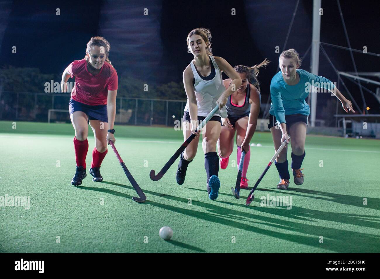 Giovani giocatori di hockey da campo femminile che corrono per la palla, giocando sul campo di notte Foto Stock