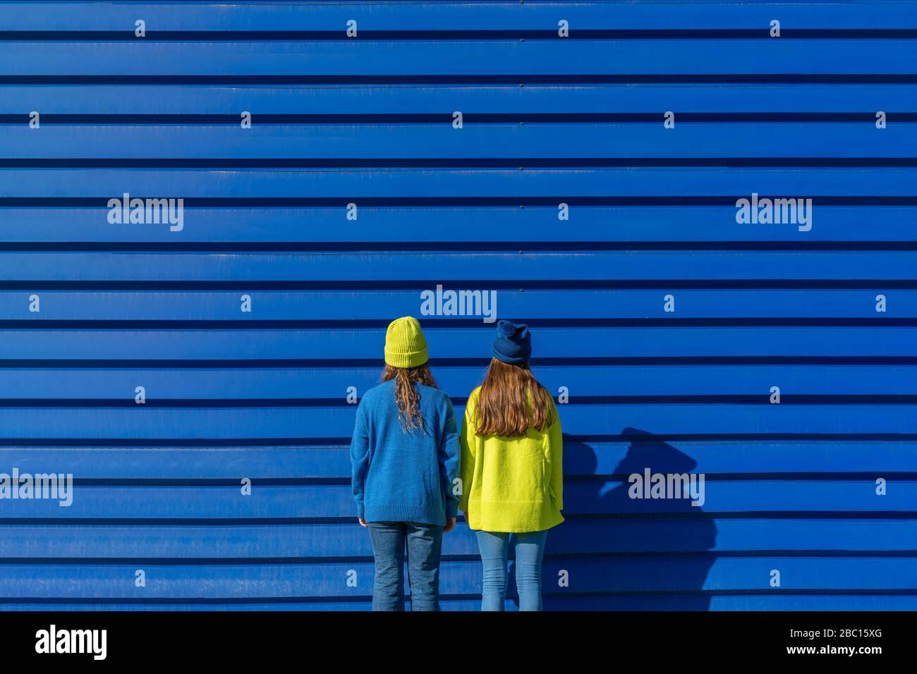 Vista posteriore di due ragazze adolescenti che indossano abiti corrispondenti in piedi di fronte a sfondo blu Foto Stock