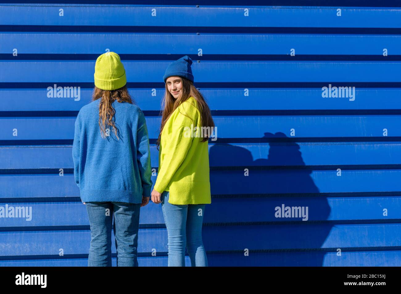 Due ragazze adolescenti che indossano abiti corrispondenti in piedi davanti a sfondo blu Foto Stock