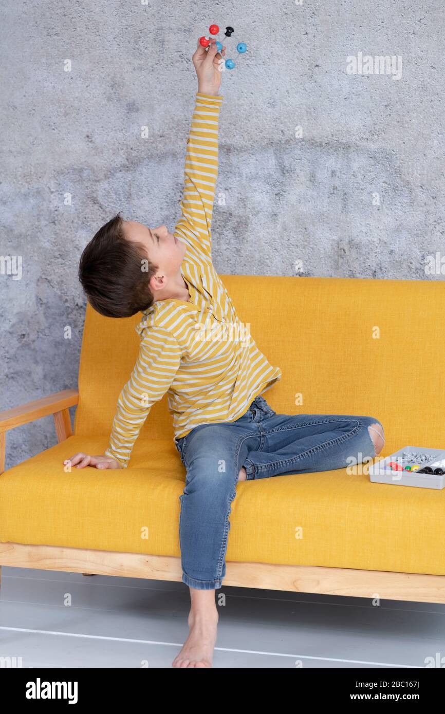 Ragazzo sta giocando e sperimentando con modelli molecolari seduti su un divano giallo Foto Stock
