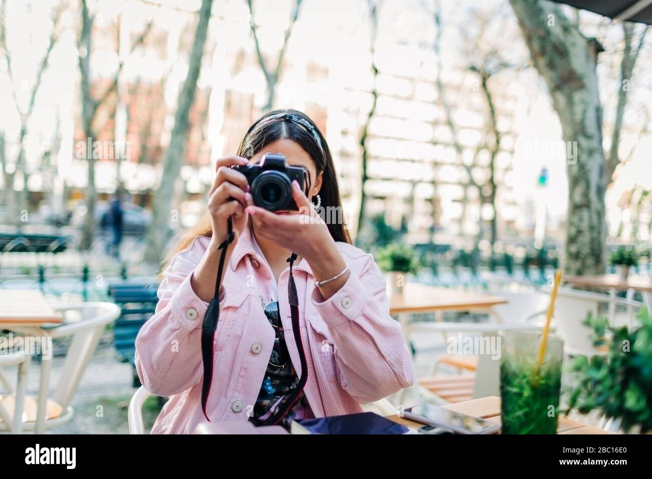 Giovane donna seduto al tavolo esterno e con una macchina fotografica Foto Stock