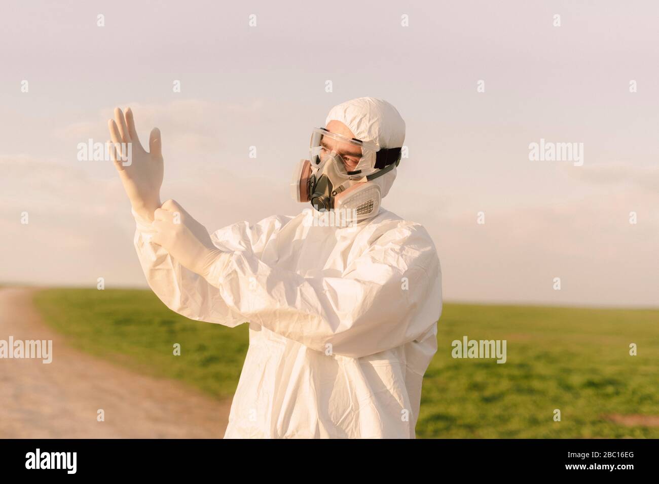 Uomo che indossa tuta e maschera di protezione in campagna indossando guanti di protezione Foto Stock